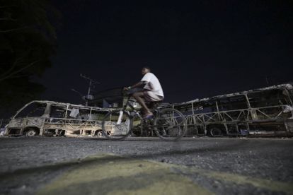 Un joven en bicicleta frente a dos de los autobuses incinerados, la noche del 23 de octubre.